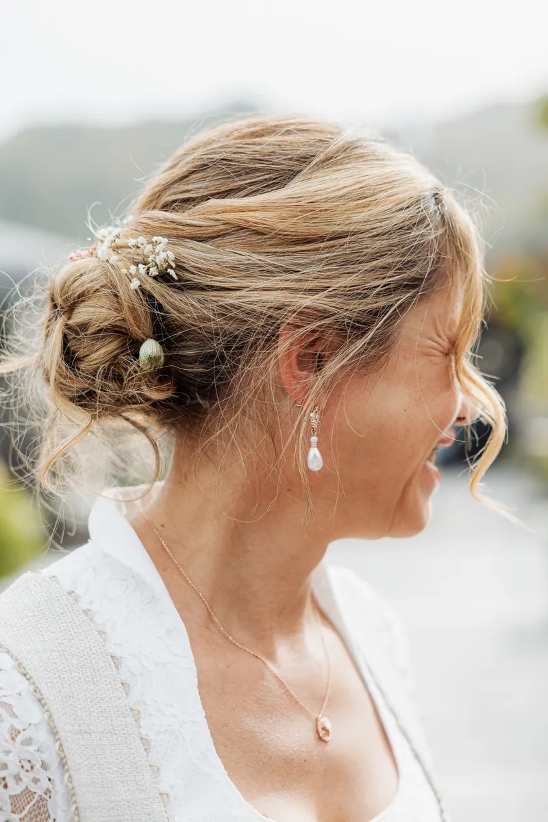 Seitenporträt einer lachenden Braut mit Hochsteckfrisur, Haarschmuck, Perlenohrring und Halskette in Spitzenkleid