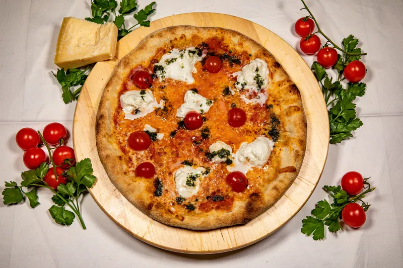 Pizza mit Burrata, Kirschtomaten und Pesto auf Holzbrett, daneben Parmesan und frische Petersilie