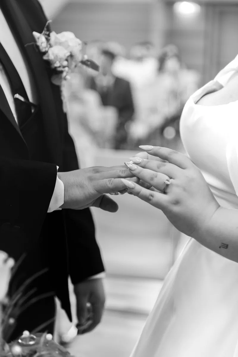 Schwarzweißaufnahme der Ringübergabe bei einer Trauung, Hände von Bräutigam und Braut im Detail